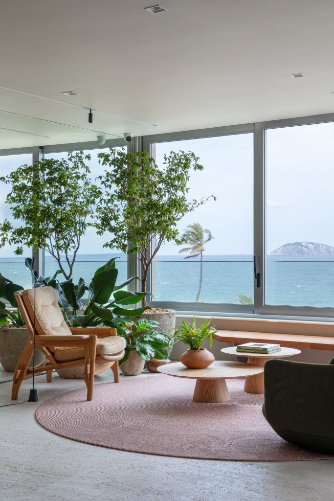 reforma-cria-coworking-sala-intima-ape-320m-up3-arquitetura-11-sala-tapete-plantas Sala de estar com grandes janelas, tapete redondo rosado, poltrona e plantas.