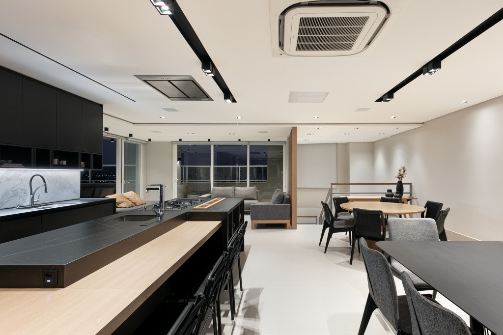 ape-275m-revestimentos-ceramicos-grandes-formatos-archilab-07 Área gourmet com marcenaria cinza escura, ilha e bancada, iluminação de spots e tv.
