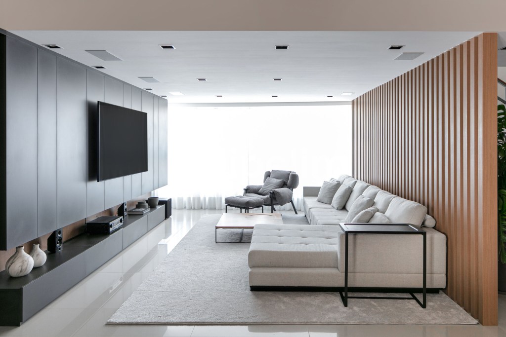 ape-275m-revestimentos-ceramicos-grandes-formatos-archilab-18 Sala com piso de porcelanato laqueado, tapete e sofá claros e parede de madeira ripada.
