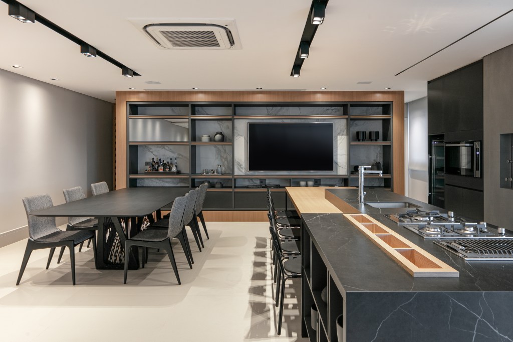 ape-275m-revestimentos-ceramicos-grandes-formatos-archilab-29 Área gourmet com marcenaria cinza escura, ilha e bancada, iluminação de spots e tv.