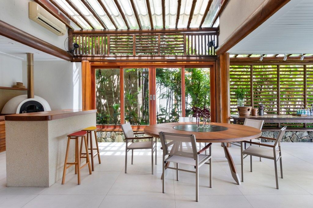 casa-400m-teto-retratil-deck-estante-embaixo-escada-11-area-gourmet Área gourmet com mesa redonda, churrasqueira, piso de porcelanato.