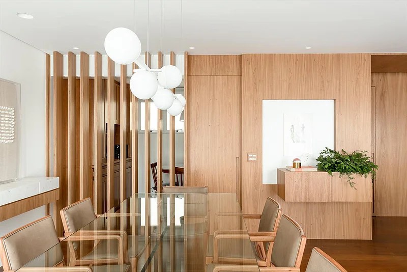 Sala de jantar com parede revestida de madeira e mesa com tampo de vidro.