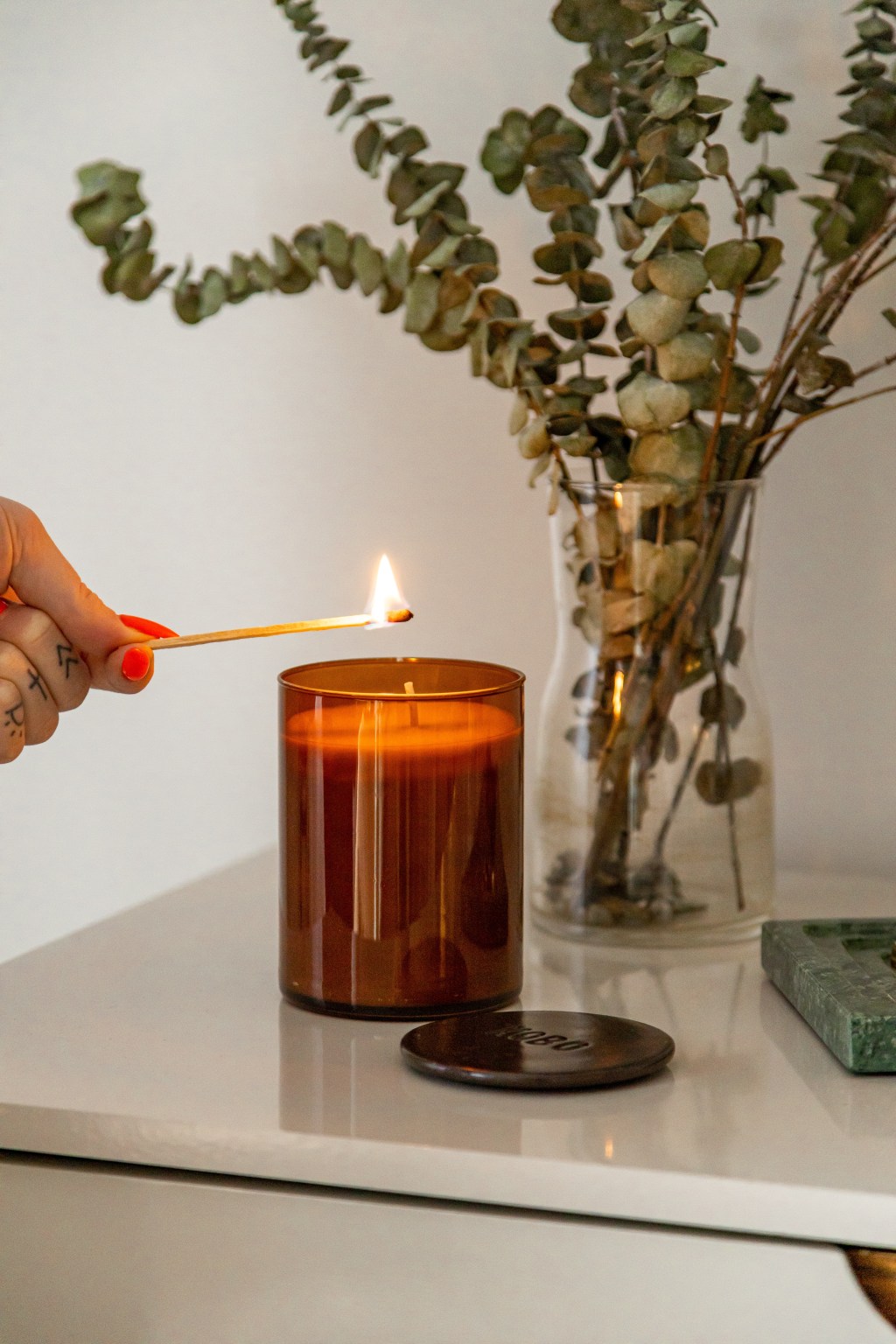 Vela aromática em mesa branca com vaso com eucalipto.