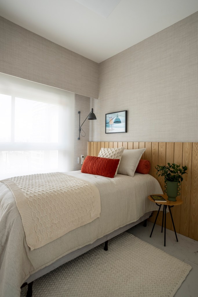 Apê de 110 m² com pé-direito duplo vira duplex com mezanino metálico Apê de 110 m² com pé-direito duplo vira duplex com mezanino metálico. Na foto, quarto de hóspedes com cabeceira de madeira e tapete.