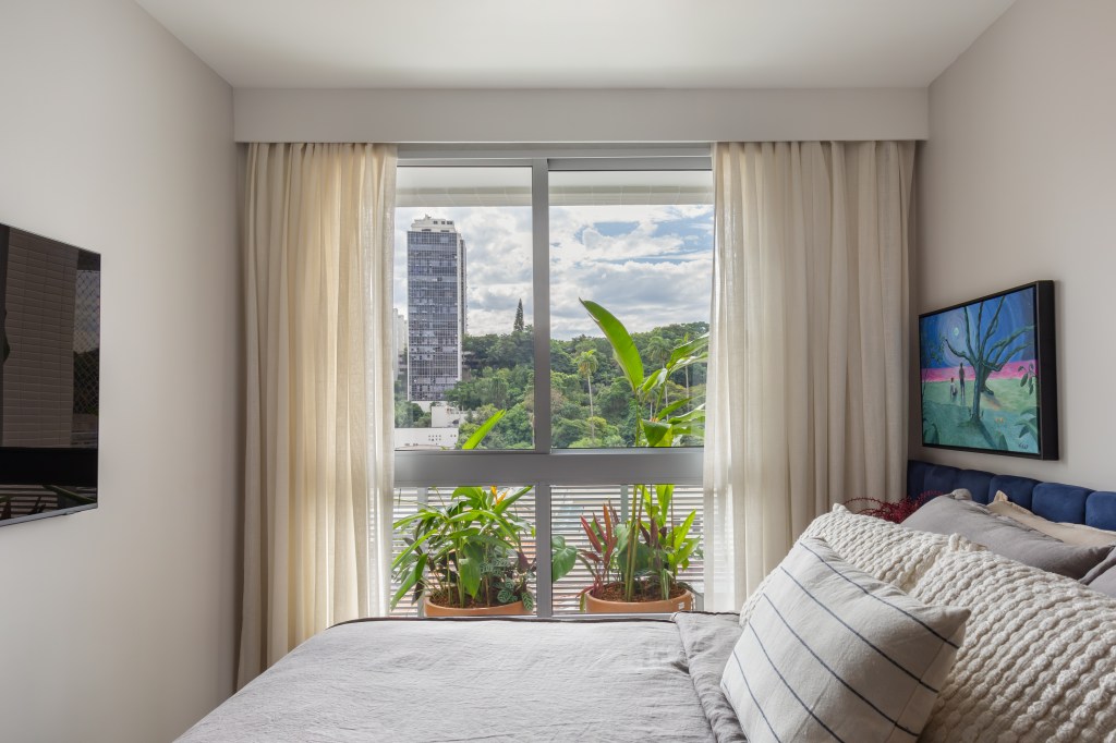 Quarto com cama de casal, quadro em cima da cama e cortina.