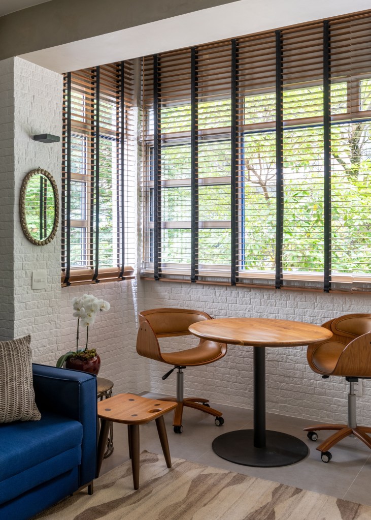 ape-90m-cozinha-com-azulejos-azuis-studio021arquitetura-14-varanda Varanda com parede de tijolinhos brancos, mesa de madeira redonda pequena e duas cadeias.
