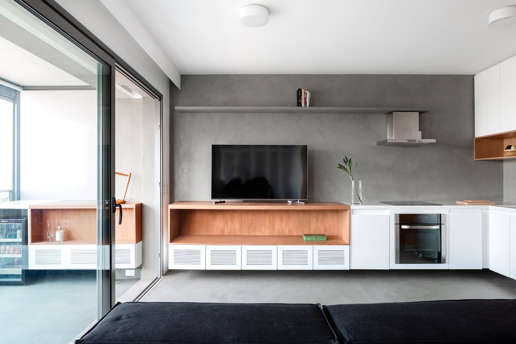 movel-usado-sofa-cama-chaise-setoriza-ape-64-m2-vaga-arquitetura-manuel-sa (1) Móvel que pode ser usado como sofá, cama ou chaise setoriza apê de 64 m². Projeto VAGA Arquitetura. Na foto, sala com cozinha integrada. Tv, sofá multiuso e varanda.