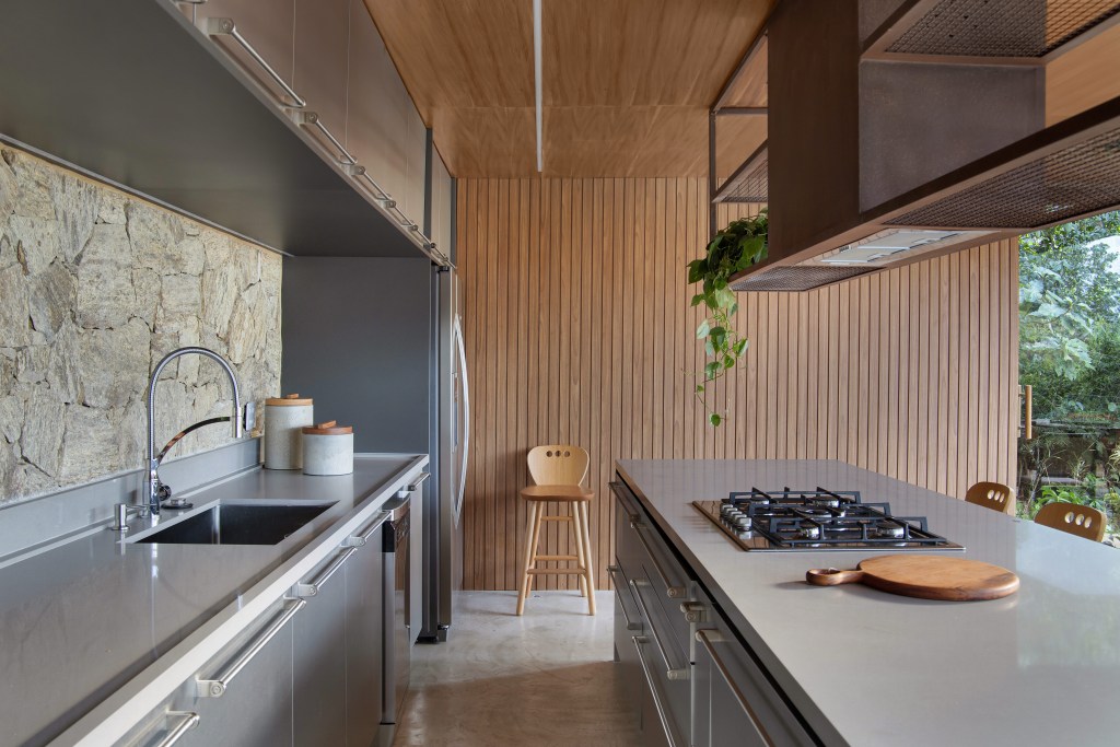 paineis-lisos-ripados-de-madeira-freijo-revestem-casa-campo-300m-diego-raposo-arquitetos-09-cozinha Cozinha integrada com marcenaria cinza e parede com ripas de madeira.