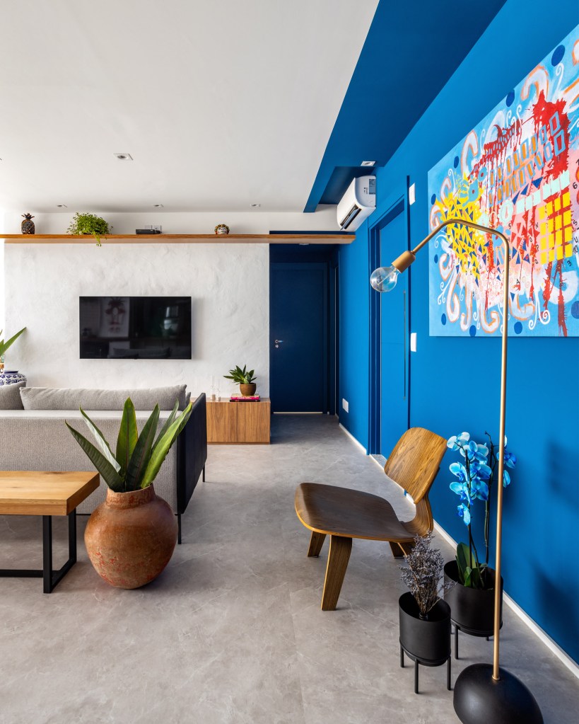 Sala de estar com parede azul, cadeira de madeira, luminária de piso