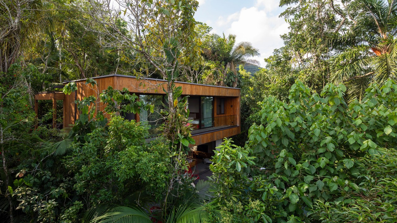 Casa de 153 m² se camufla em meio à natureza do litoral paulista. Projeto de Daniel Fromer, interiores de Julyana Bortolotto. Na foto, fachada da casa em meio à mata nativa.