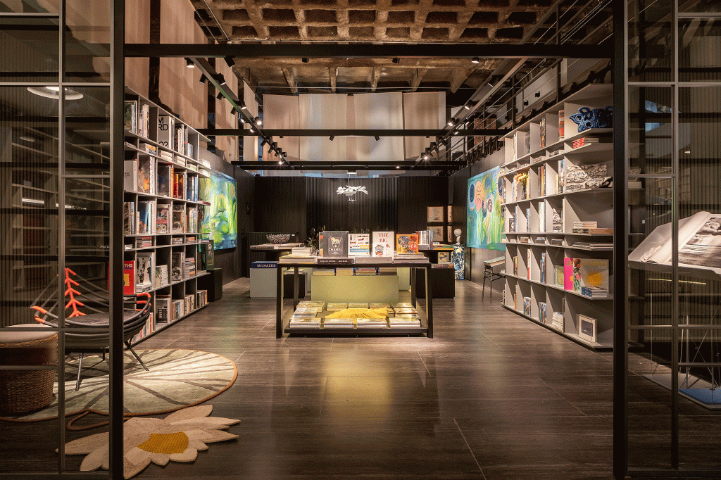 Esta livraria tem clima intimista e repleta de arte brasileira. Projeto de Nana Cunha, Caru Cunha e Sílvia Camargo para a CASACOR SP 2023. Na foto, estantes com livros, paredes escuras e quadros.