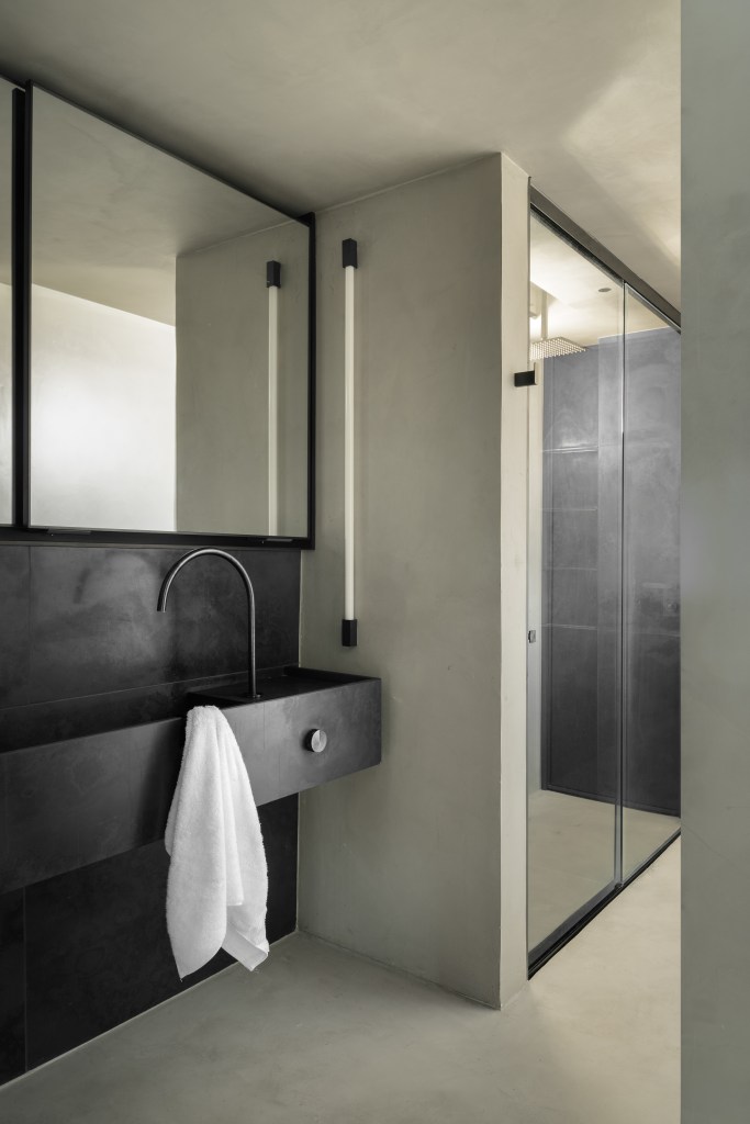 Minimalista: apê de 300 m² utiliza poucas cores e efeitos de luz no décor. Projeto de Lucas Lage. Na foto, banheiro com bancada preta e espelho.