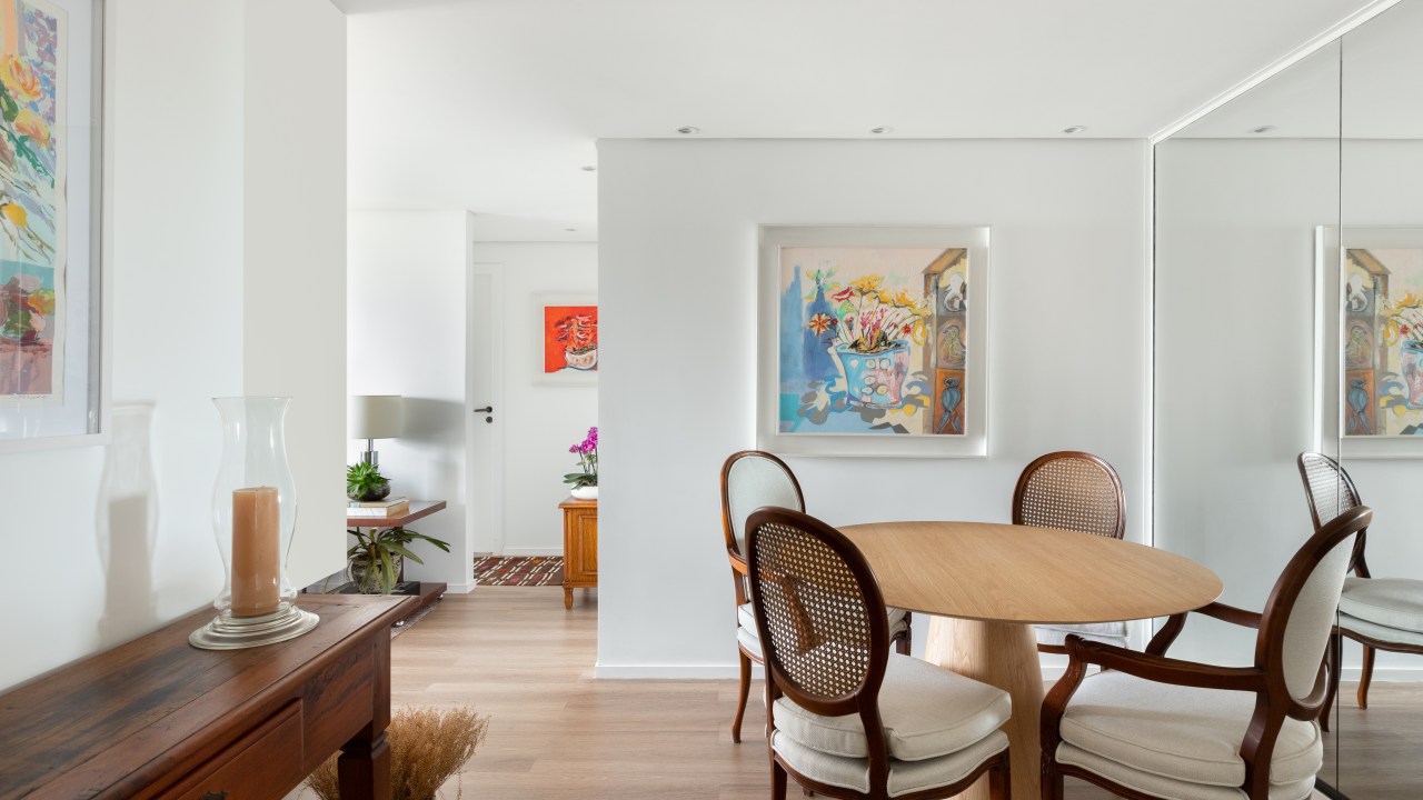 Sala de jantar com mesa redonda de madeira, cadeiras em estilo medalhão e parede com espelhos.