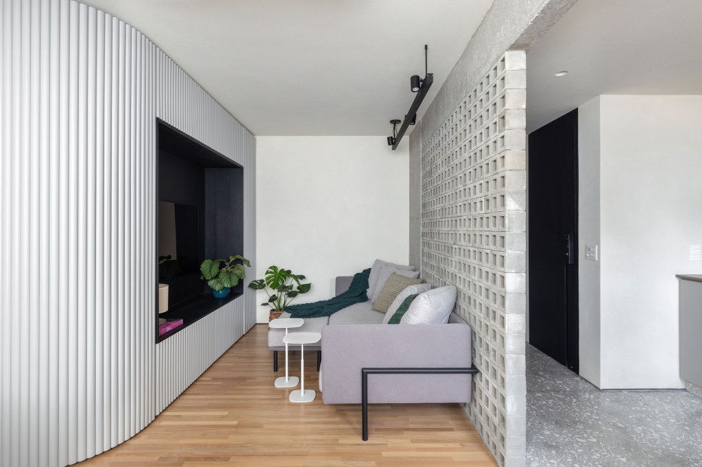 Sala de tv; sala de estar com painel ripado cinza, sofá cinza e painel vazado de concreto.