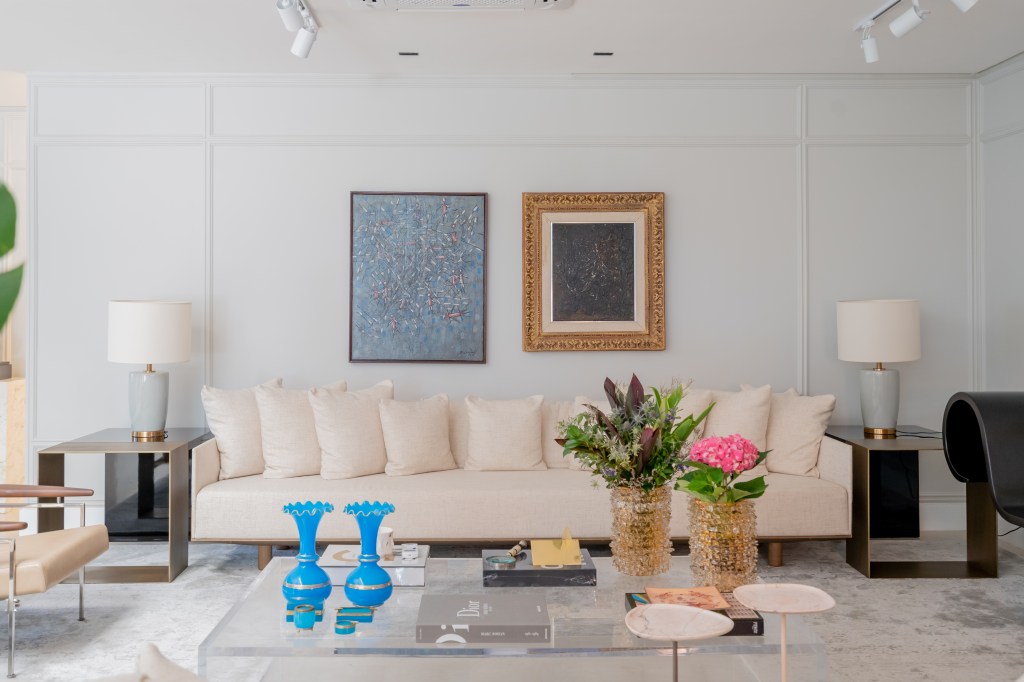 casa-785m-digital-influencer-salao-de-beleza-rosa-romario-rodrigues-arquitetos-08 Projeto de Romário Rodrigues Arquitetos. Na foto, sala de estar branca com sofá branco e parede com boiseries e quadros.