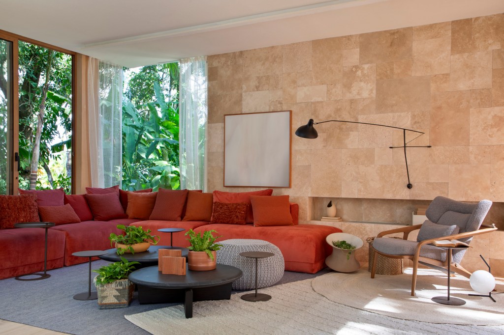 casa-de-campo-105-m2-meio-natureza-tres-conteineres-up3-arquitetura-credito-denilson-machado (7) Casa de campo de 105 m² no meio da natureza é feita com três contêineres. Projeto de Up3 Arquitetura para a CASACOR Rio de Janeiro 2023, Na foto, sala e estar com sofá vermelho e parede de vidro.