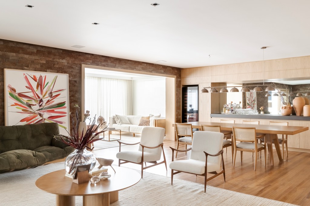 Apartamento Vila Nova Conceição Tijolinhos revestem todas as paredes do living deste apê de 310 m². Projeto de Très Arquitetura. Na foto, sala de estar e jantar com parede de madeira e poltronas.