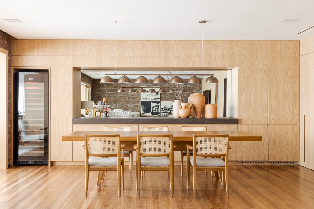 Apartamento Vila Nova Conceição Tijolinhos revestem todas as paredes do living deste apê de 310 m². Projeto de Très Arquitetura. Na foto, sala de jantar com cadeira de palhinha, espelho e bar.