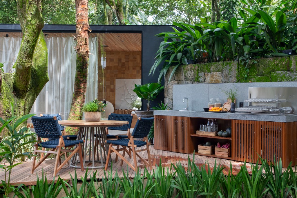 Refúgio do Lago - ambiente de Leila Dionizios. Na foto, área externa com área gourmet com mesa, cadeiras e bancada de cozinha.