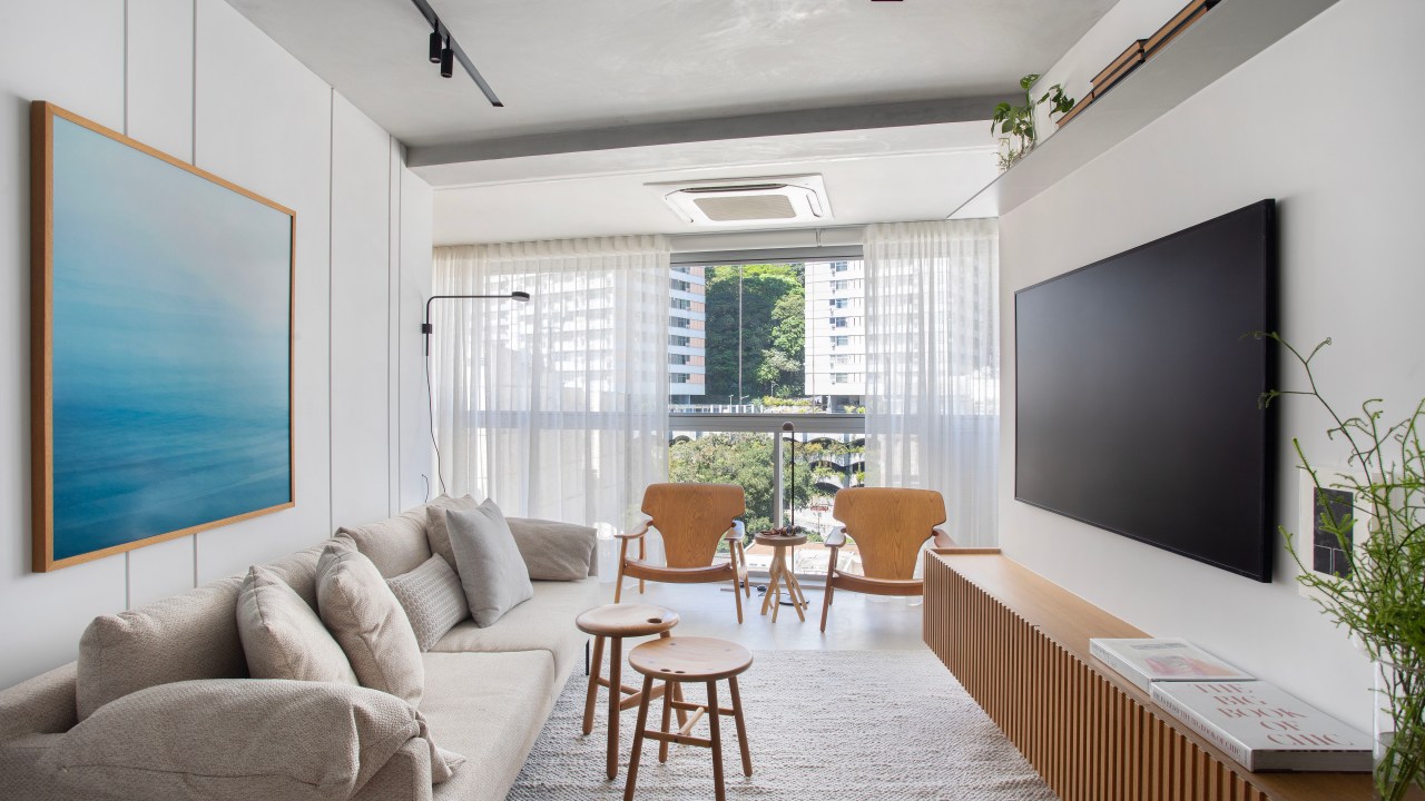 Apê neutro de 90m² aposta em porcelanato off white e cinza nos banheiros. Projeto de Rafael Ramos. Na foto, sala neutra com sofá off white e rack de madeira.