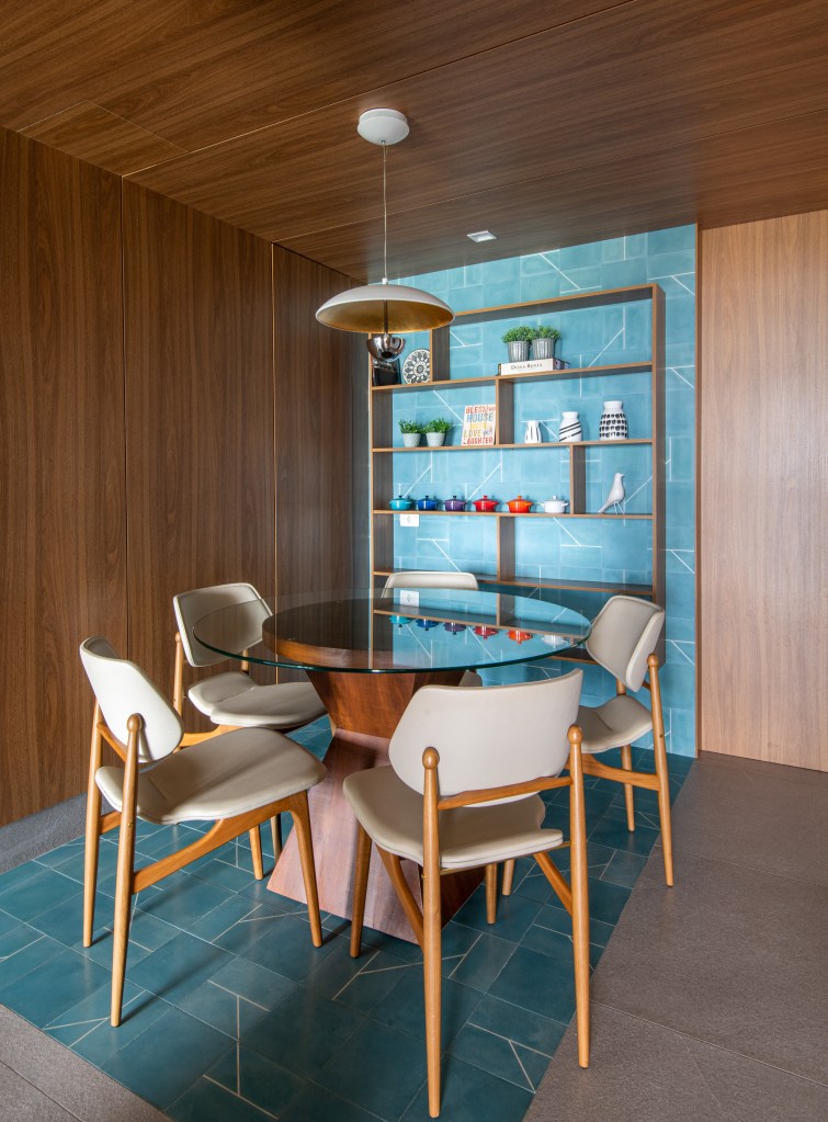 © Favaro JR Forro iluminado de muxarabi cria sensação de luz natural em apê de 278 m². Projeto de Cris Furlan. Na foto, sala de almoço com mesa de vidro e piso e parede azuis.