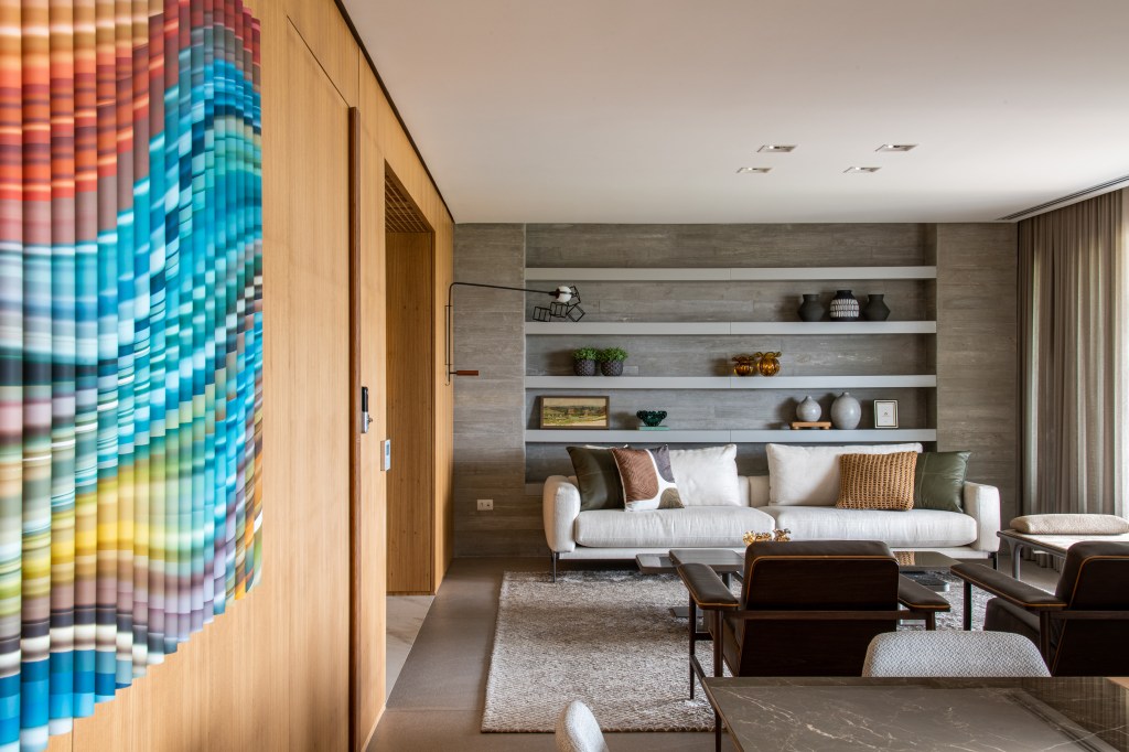 © Favaro JR Forro iluminado de muxarabi cria sensação de luz natural em apê de 278 m². Projeto de Cris Furlan. Na foto, sala de estar com estante embutida e parede de madeira.