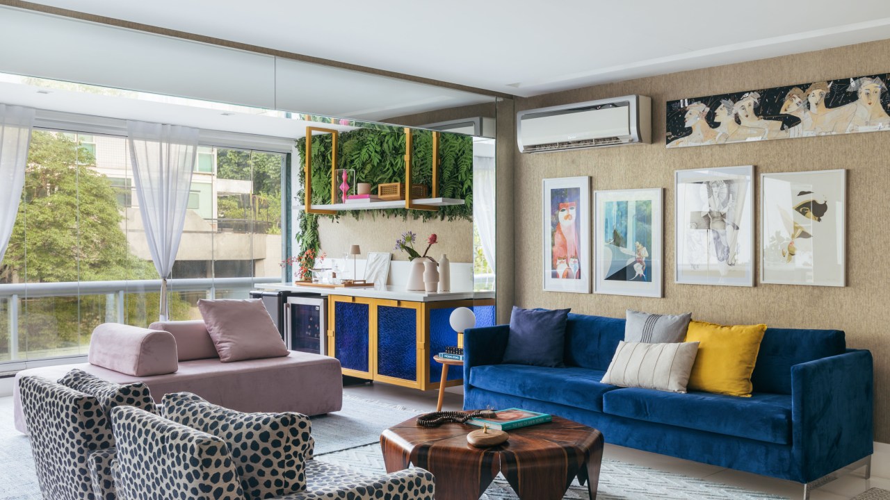 Apê de Ciro Bottini tem paleta Art Deco Navy com tons azuis e dourados. Projeto de Casa Cururu. Na foto, sala integrada com varanda com sofá azul, rosa e poltrona com estampa animal.