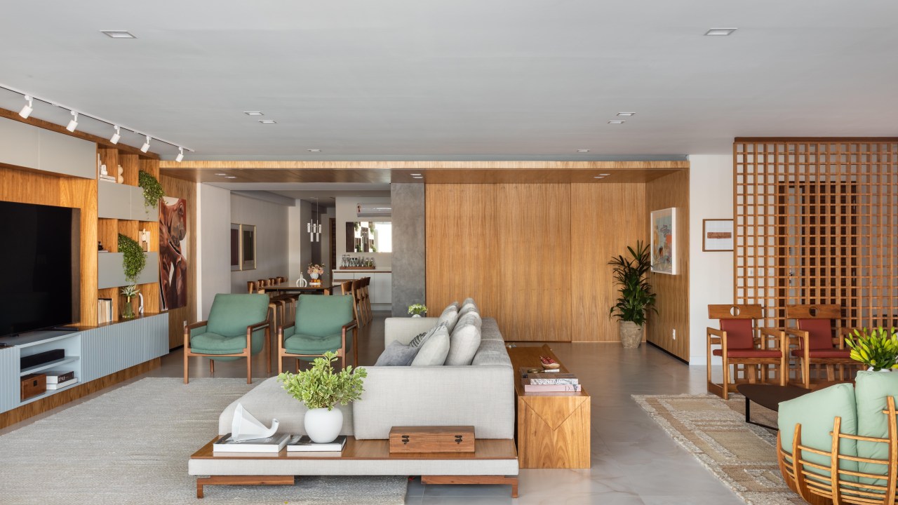 Apê de 270m² ganha piso de porcelanato marmorizado e sala íntima. Projeto de Henrique Ramalho. Na foto, sala integrada com piso de porcelanato, porta de correr de madeira e sofá cinza.