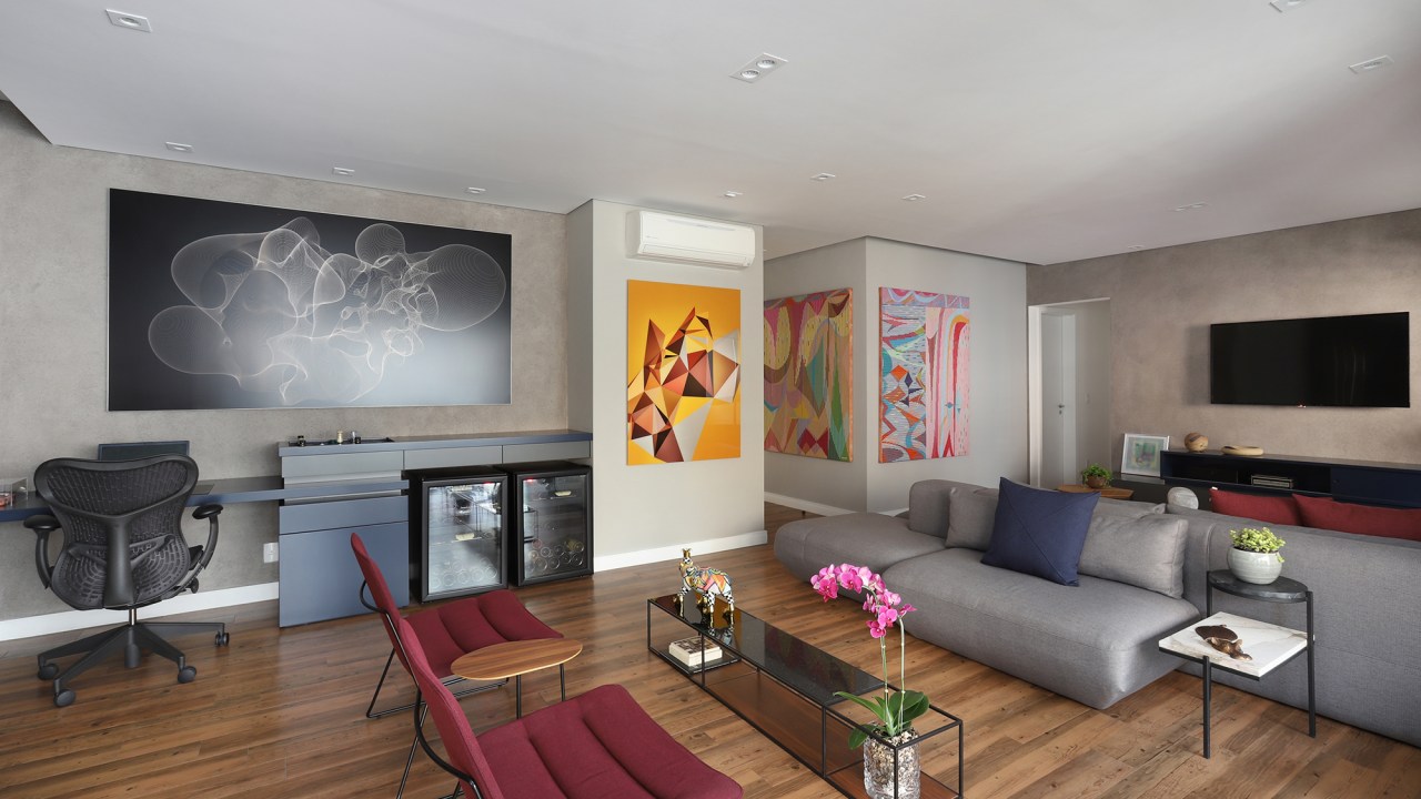 Apê descolado de 120 m² tem décor inspirado nos quadros do cliente. Projeto Inovando Arquitetura. Na foto, sala com sofá ilha cinza, quadros e parede de cimento queimado.