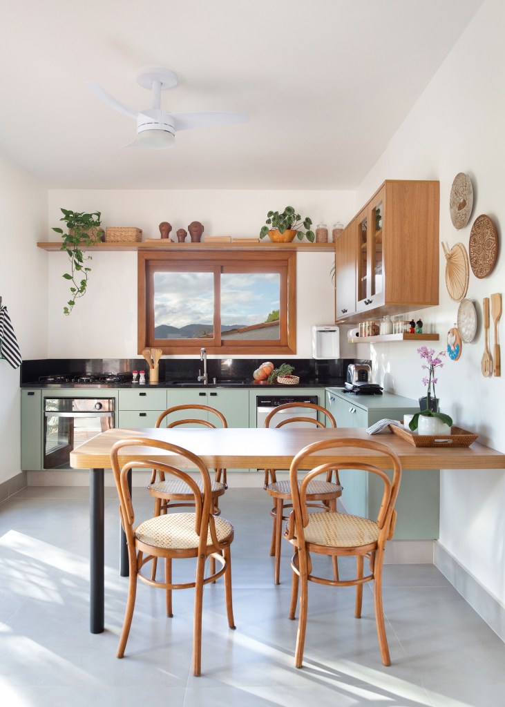 Cozinha de 15m² tem estilo contemporâneo com toque campestre. Projeto de Travessa Arquitetura. Na foto, cozinha com copa, bancada preta e armários verde claros.