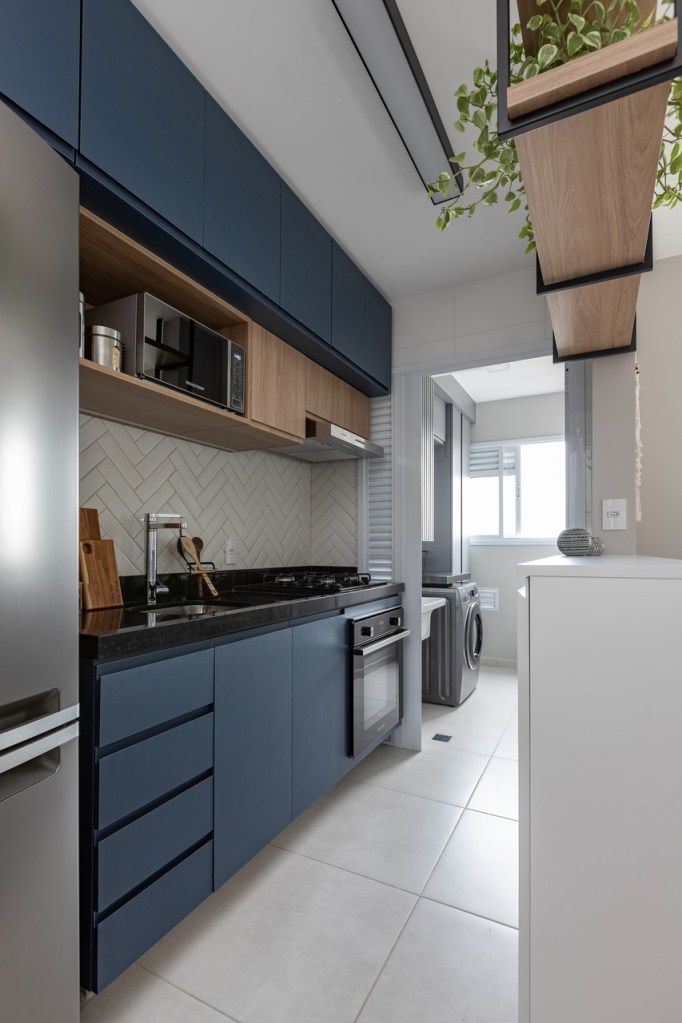 Sem quebra-quebra, apê de 53 m² ganha cores e canto alemão com sapateira. Projeto de Studio Monfré. Na foto, cozinha integrada com marcenaria azul e backsplash chanfrado.