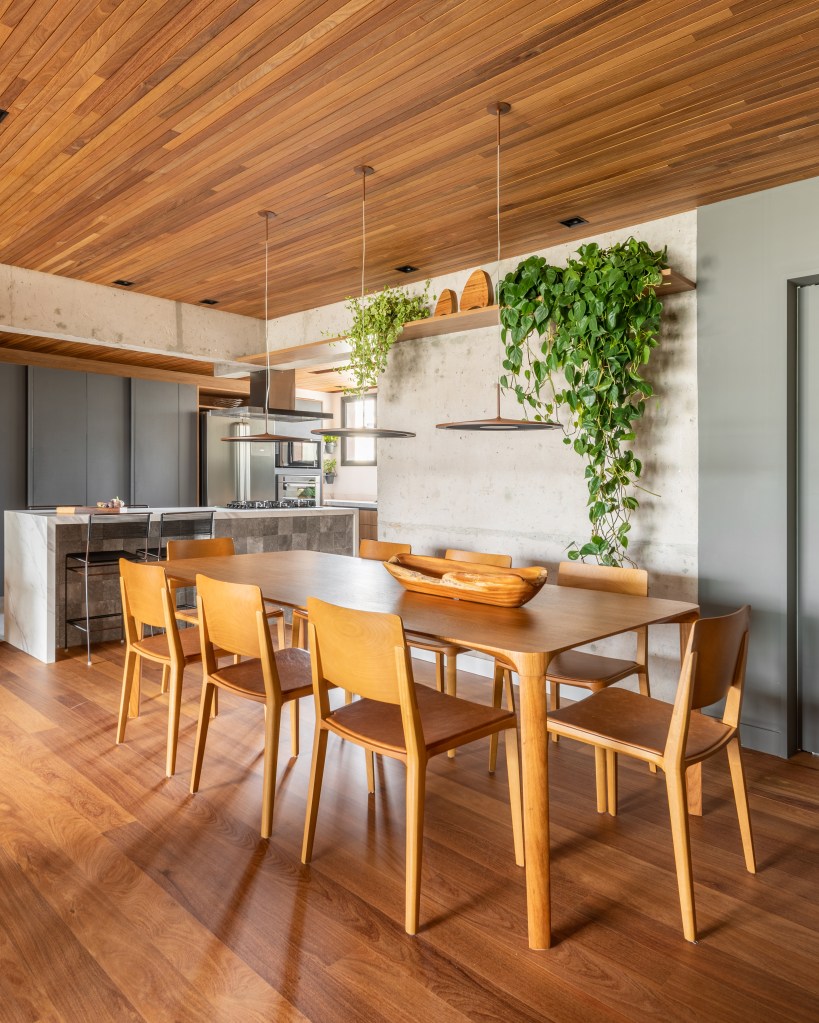 Cozinha integrada com bancada de neolith e cristaleira é destaque em apê. Projeto de Pietro Terlizzi. Na foto, sala de jantar com mesa de 8 lugares, integrada com cozinha. Prateleira com plantas.