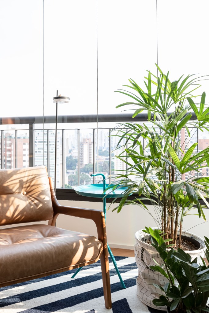 painel-rack-tv-separam-living-home-office-ape-75m-ilse-arquitetura-04-varanda-plantas Painel e rack de TV separam living de home office em apê de 75m². Projeto de ISE Arquitetura. Na foto, varanda com tapete azul e branco e poltrona.