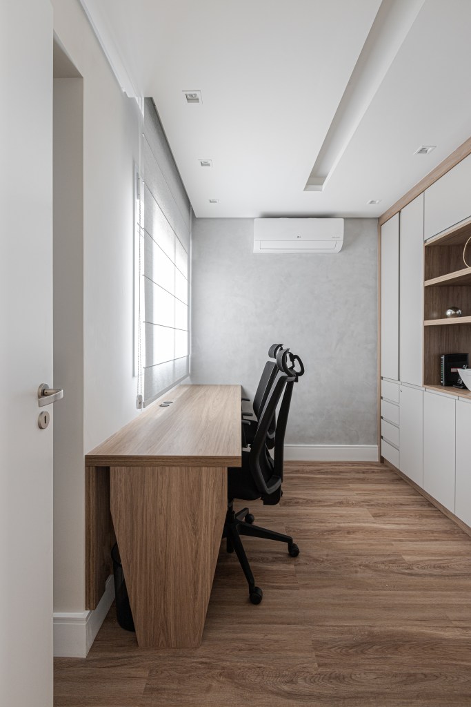 Reforma em apê de 140m² transforma banheiro em biblioteca de home office. Projeto de Blaia e Moura Arquitetos. Na foto, home office com bancada de madeira, duas cadeiras e estante de marcenaria branca.