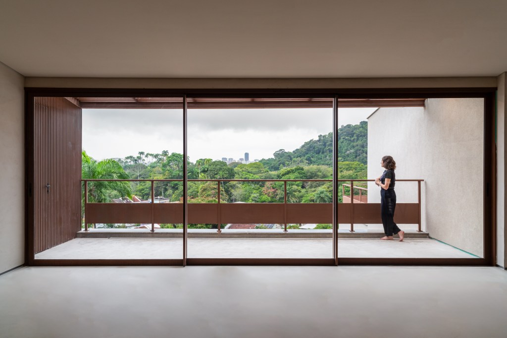 No terreno em declive, casa preserva a memória da arquitetura original. Projeto Cité Arquitetura. Na foto, sala com terraço e vista para a natureza.