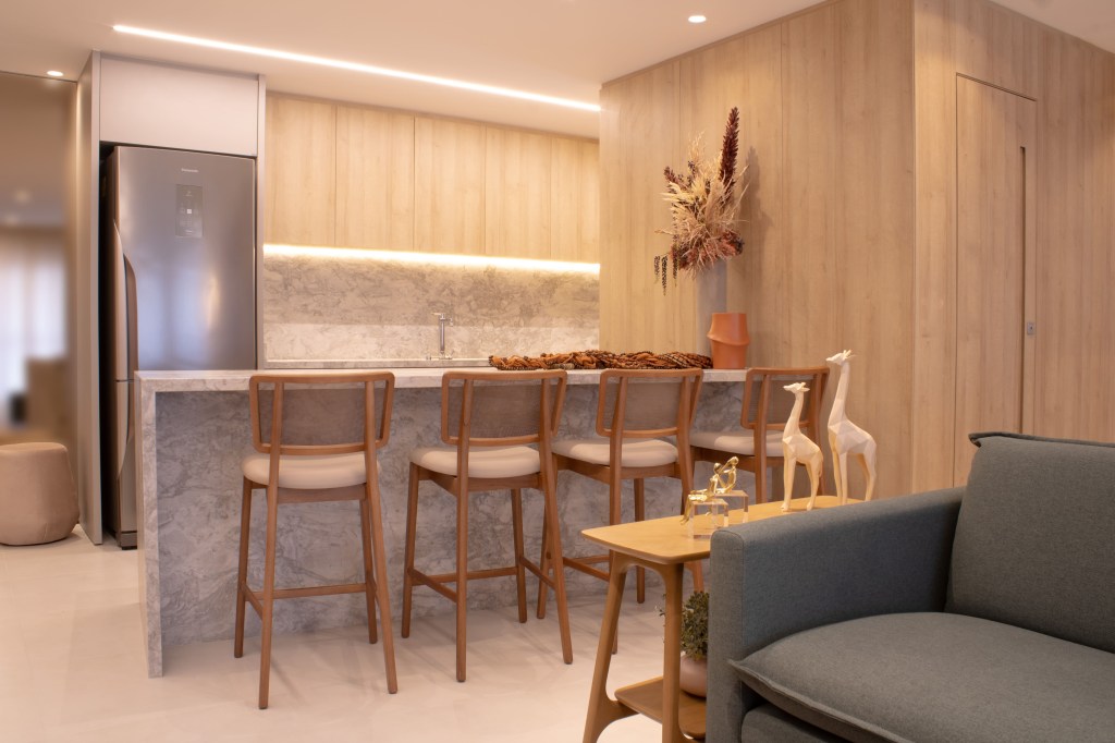 Apartamento de 80 m² ganha lareira a gás e parede marsala na sala. Projeto do arquiteto Felippe Comninos, à frente da Vale Arquitetura, em parceria com a arquiteta Adriana Marcassa Cotrin, do escritório Marcassa Cotrin. Na foto, sala com cozinha americana e balcão com textura de pedra.