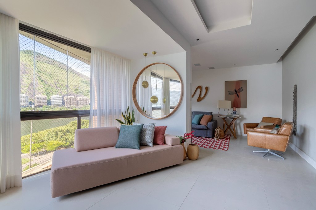 Apê ganha mezanino com home office, lavabo azul e copa de cozinha turquesa. Projeto de Ana Cano Arquitetura. Na foto, sala de estar, sofá rosa claro, espelho redondo.