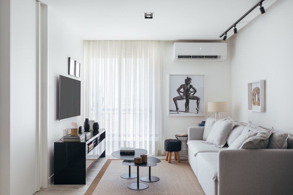 Estilo escandinavo inspira décor de apê de 84m² com paleta preta e branca. Projeto de Nilton Montarroyos. Na foto, sala de estar com sofá cinza claro, rack preto, mesa de centro preta e ar condicionado.