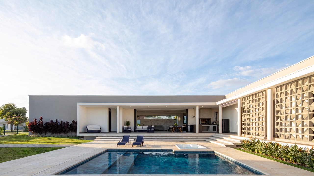 Fachada de cobogós cria efeito cênico nesta casa no interior de São Paulo. Projeto de Starq, Na foto, fachada da casa com piscina e jardim.