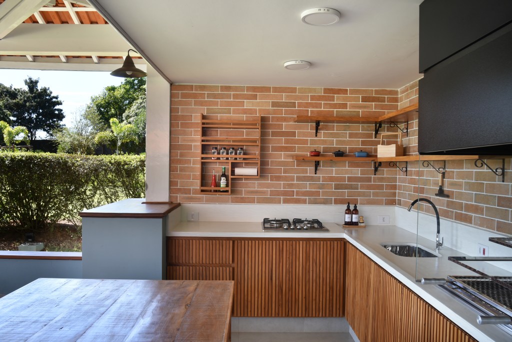 Rústico chic: casa de campo tem orquidário e cozinha com cara de fazenda. Projeto de Rosangela Pena. Na foto, área gourmet com parede de tijolinhos, bancada branca, cooktop.