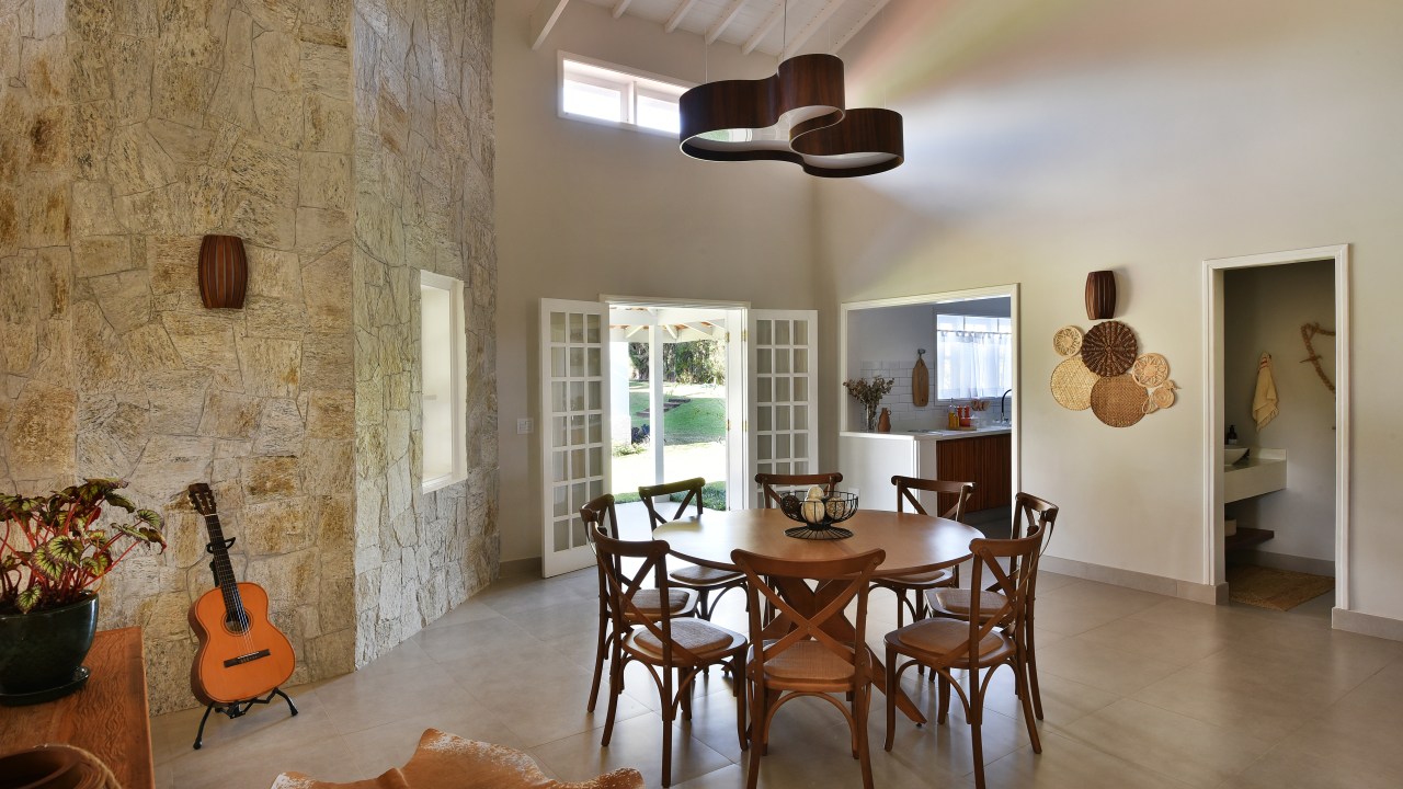 Rústico chic: casa de campo tem orquidário e cozinha com cara de fazenda. Projeto de Rosangela Pena. Na foto, sala de jantar com pé direito duplo, mesa redonda de madeira e luminária.