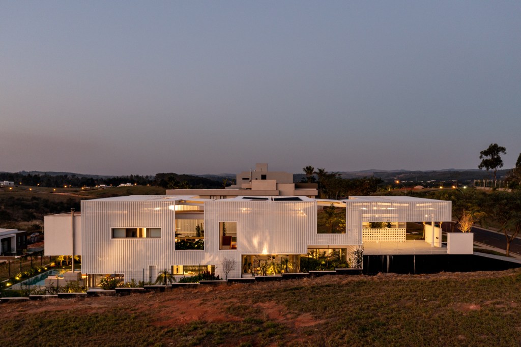 Treliças brancas de metal compõem a fachada desta casa em Campinas. Projeto de FGMF. Na foto, vista da fachada à noite.