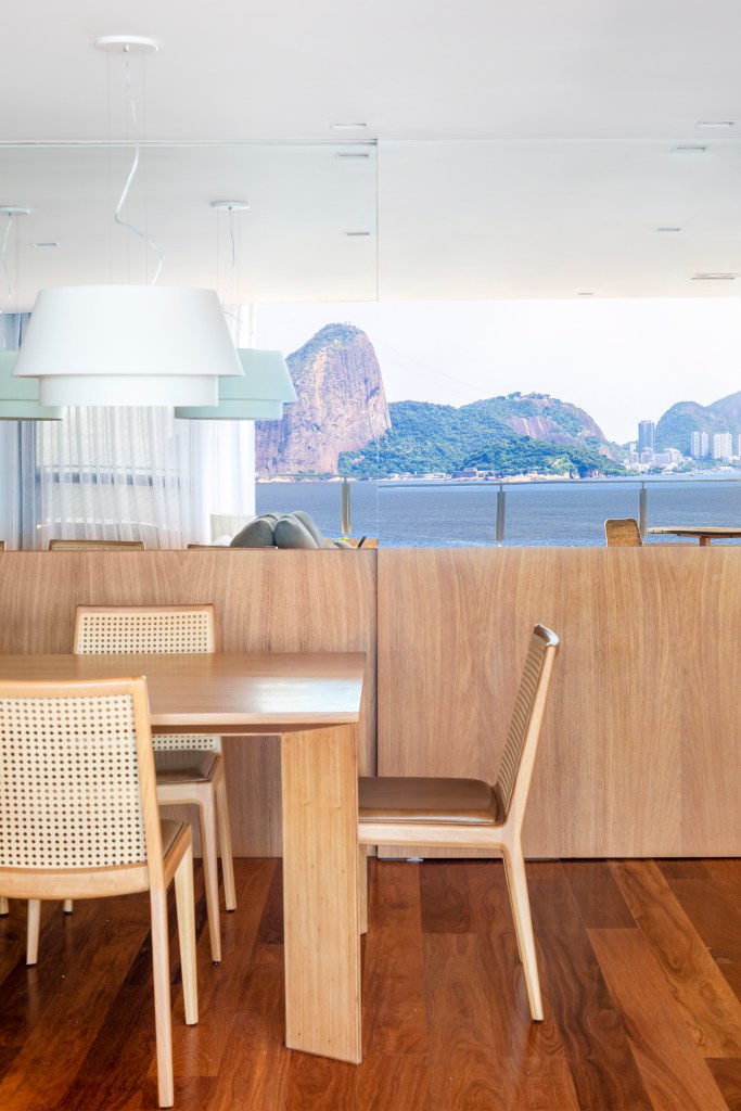 Apê de 300 m² tem sala íntima com TV e cozinha com armários amarelos. Projeto de PKB Arquitetura. Na foto, sala de jantar com vista para pão de açúcar, mesa e cadeiras de madeira.