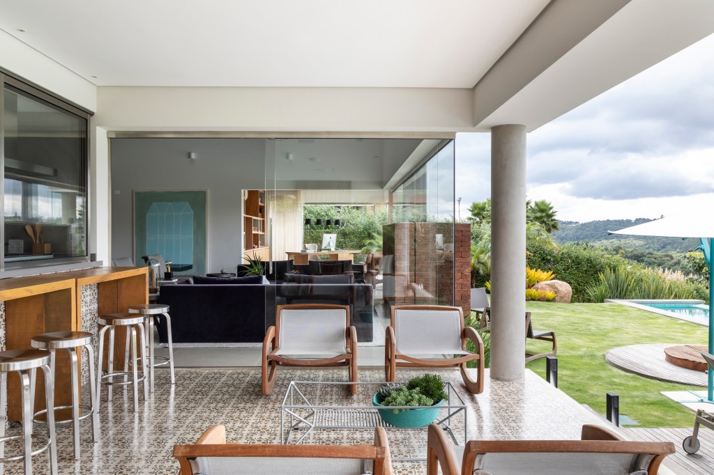 Atemporal e elegante: casa tem lareira e cozinha com piso de ladrilho. Projeto de Carolina Gava. Na foto, sala de estar integrada com varanda gourmet.