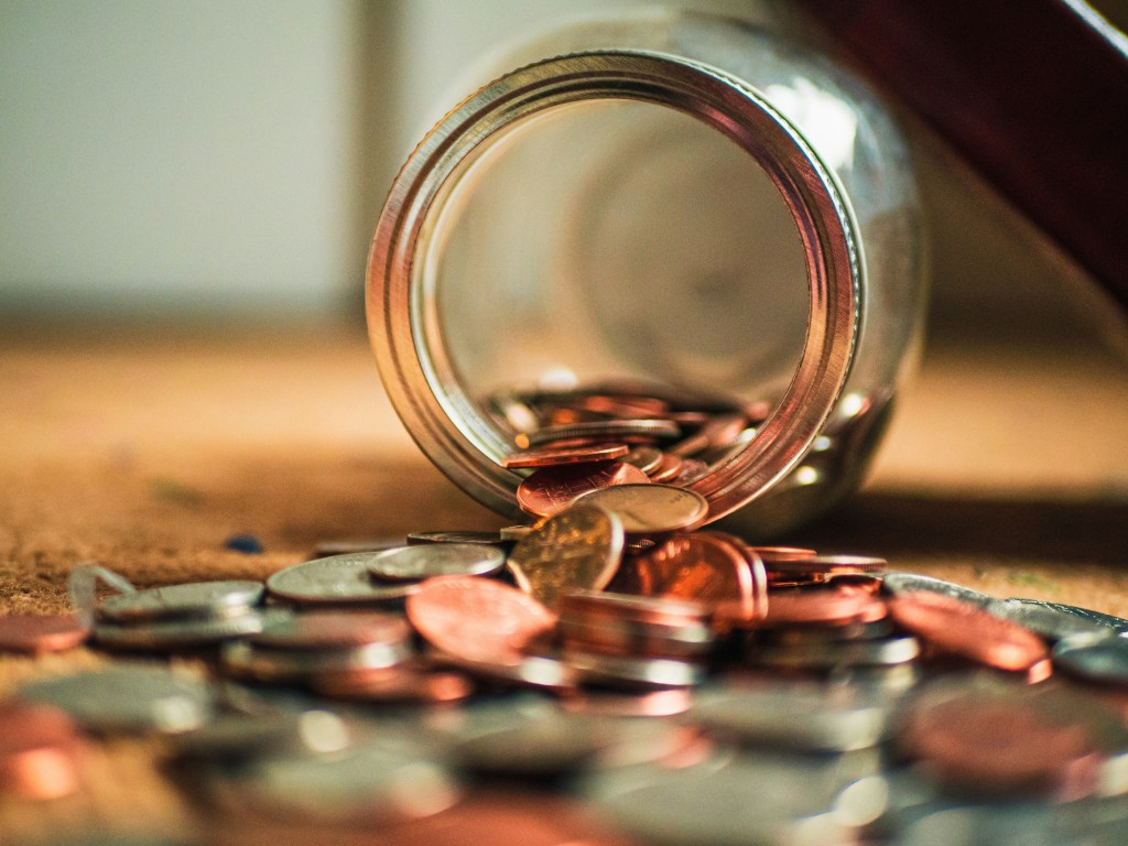 Como fazer um ritual para atrair mais dinheiro. Na foto, pote vidro com moedas virado em mesa.