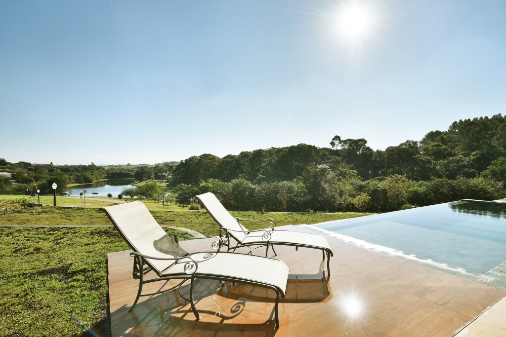 Grandes aberturas realçam o décor clean desta casa de veraneio com piscina. Projeto de Marcela Rocca. Na foto, piscina e espreguiçadeiras.