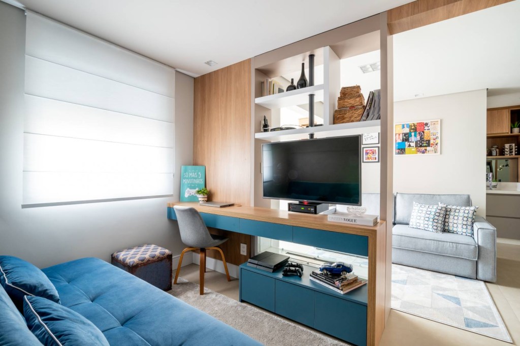 Painel com TV giratória divide  sala de home office neste apê