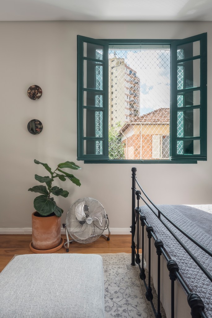 Sobrado de 100 m² ganha solarium e décor que é mix de rústico e retrô. Projeto de Palladino Arquitetura. Na foto, quarto com janela colorida, planta e ventilador de piso.