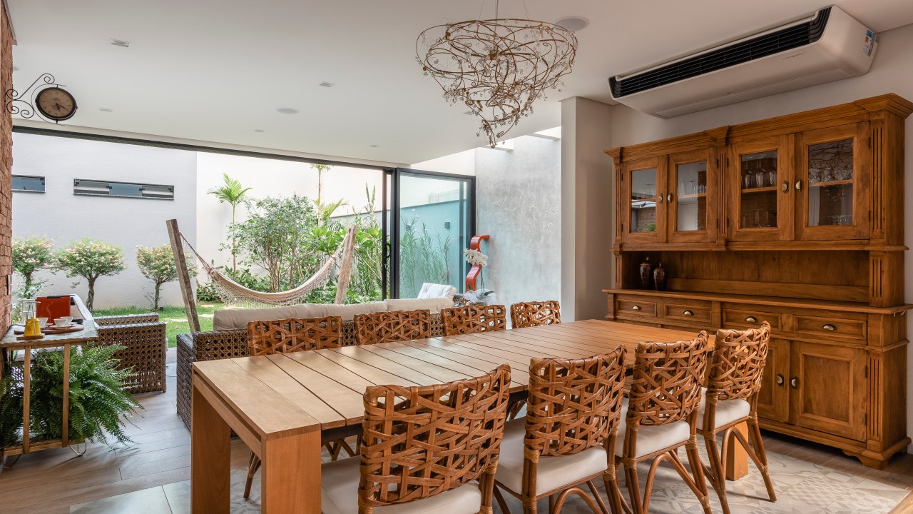 Estilo rústico chic com madeira é tendência na decoração. Projeto de Patrícia Penna. Na foto, sala de jantar com mesa rústica de madeira, cadeiras de madeira e portas de correr de vidro para o jardim.