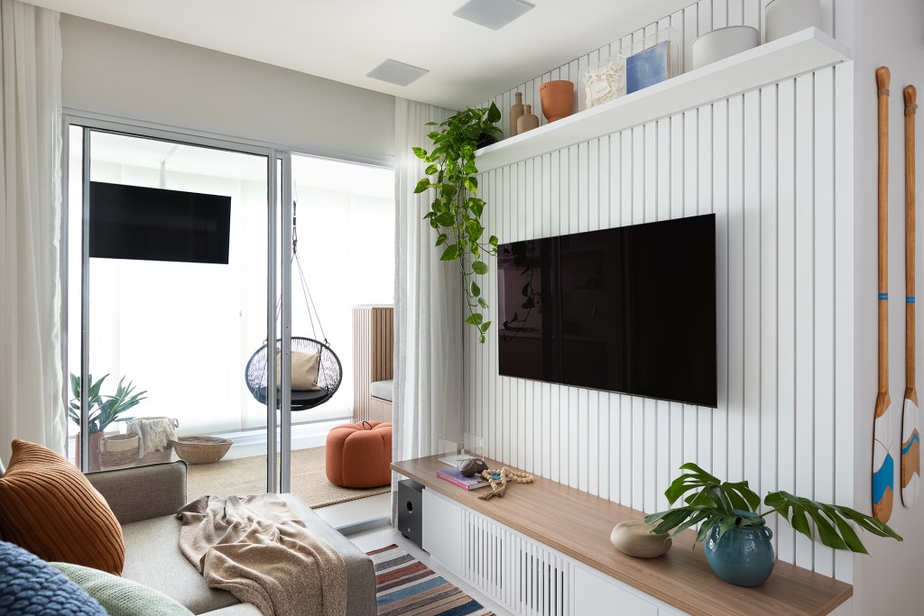 Apartamento de 83 m² ganha décor acolhedor sem derrubar nenhuma parede. Projeto do Estúdio Maré, Na foto, sala de estar com parede ripada e varanda com balanço.